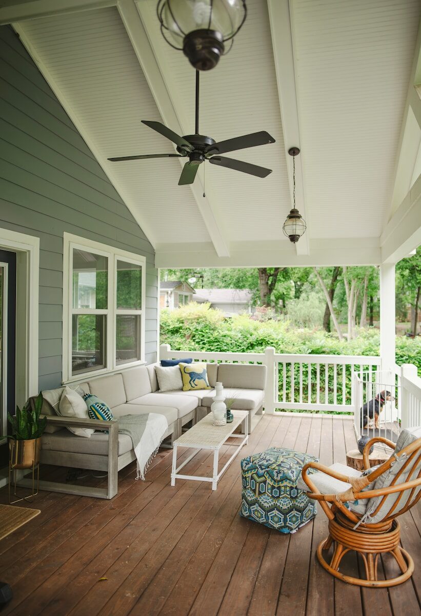 A porch with a couch, chairs and a ceiling fan